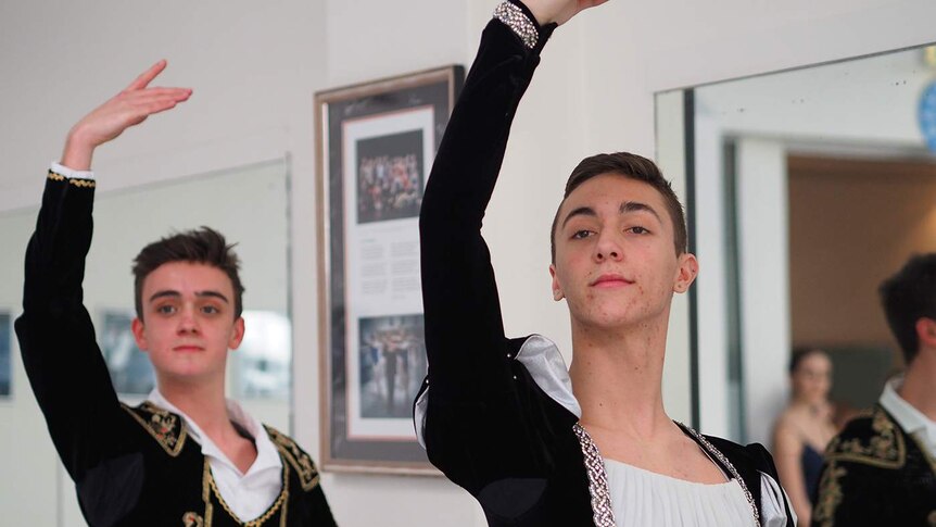 Two male ballet dancers in black jackets posing next to one another.