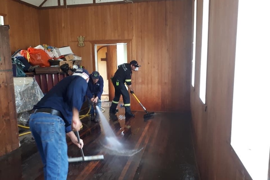 Two volunteers holding hoses and cleaning out a flooded building