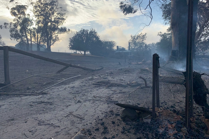 Burnt fences, trees and farmland with a house in the background