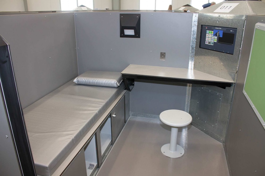 Prison cell that includes partition-style walls, bed, desk and an audio visual entertainment system.