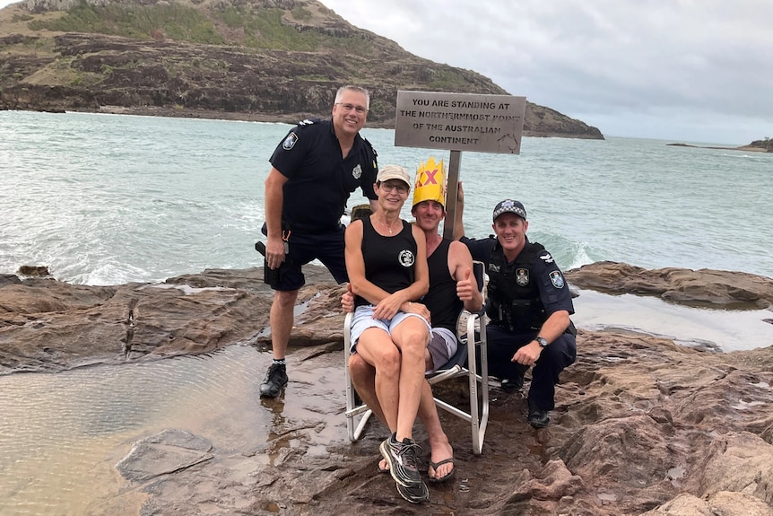 two male police officers and a male and female couple on a rocky area with sea in the background