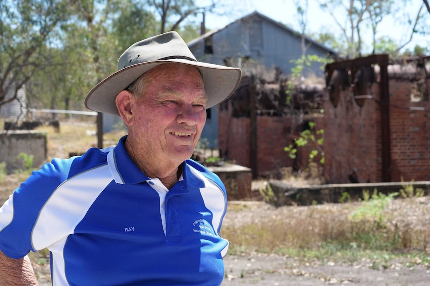 An older man stands in front of historic mine buildings