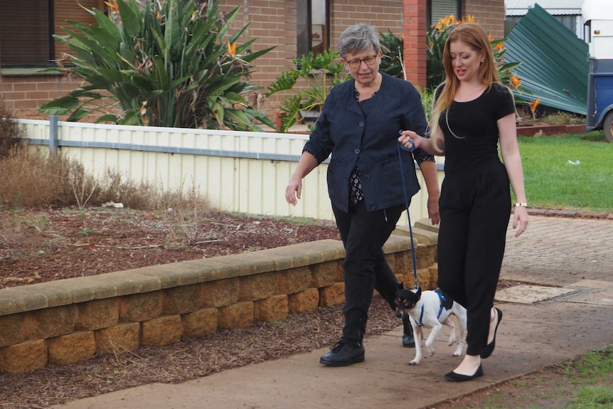 Two woman walk along a footpath walking a jack russell dog