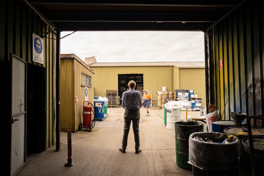 An older man looks out of a factory doorway.