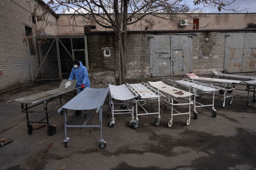 A line of stretchers outside a mortuary with a worker wheeling one.
