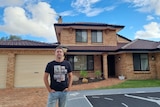 Recent home buyer Denis Barnard standing in front of a house with a blue sky behind.