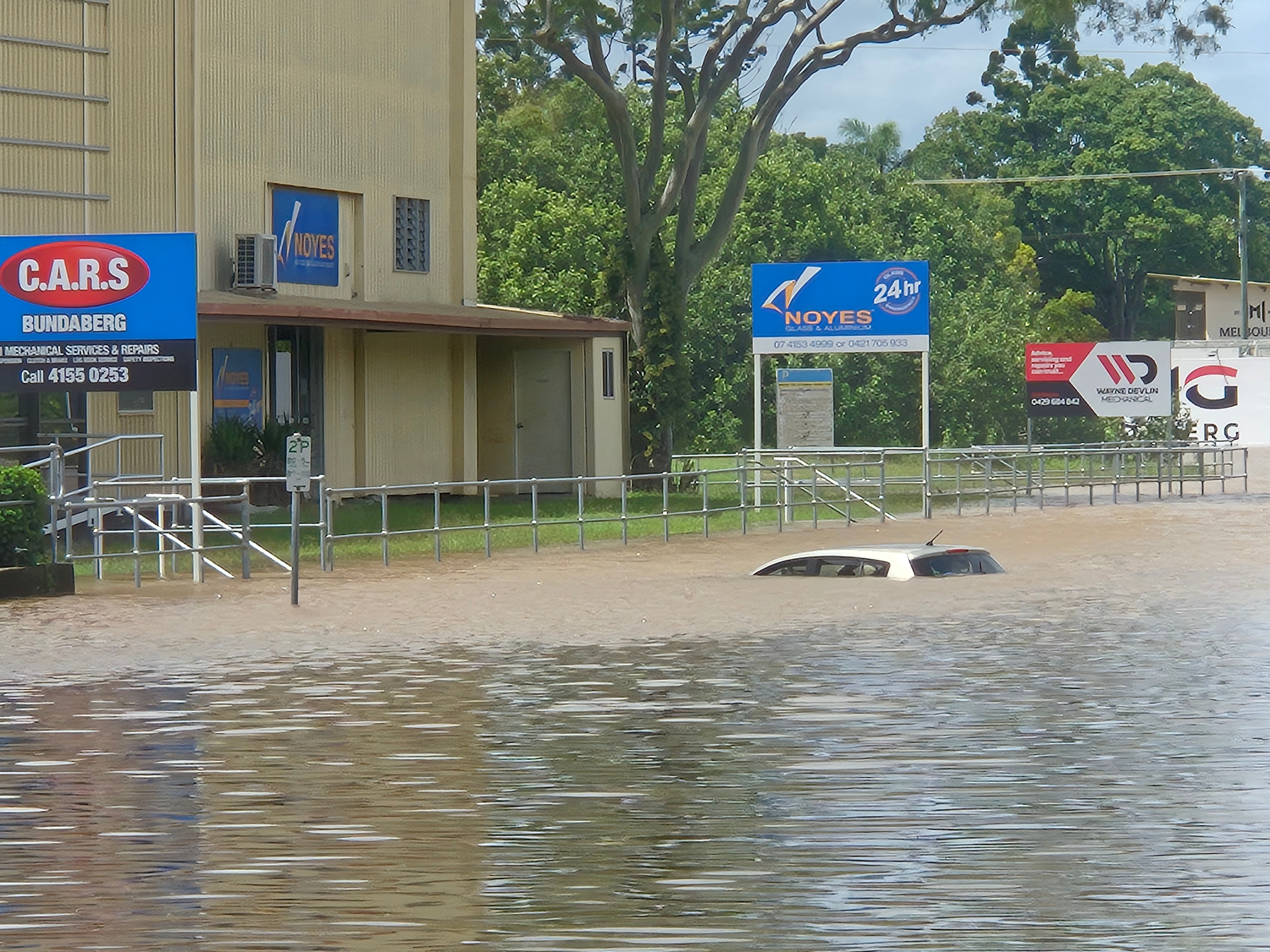 A car underwater up to its roof in front of a business.