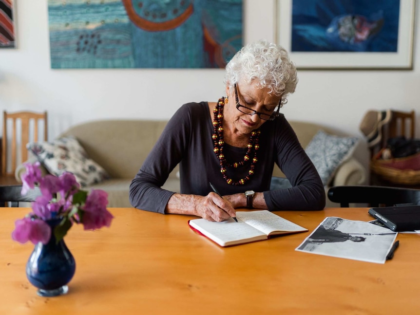 Professor Fiona Stanley writes in a notebook at a desk.