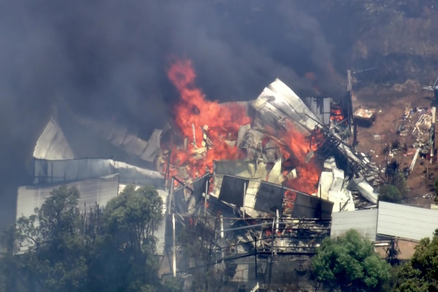An aerial image of a house on fire and partially collapsed in a semi-rural area.