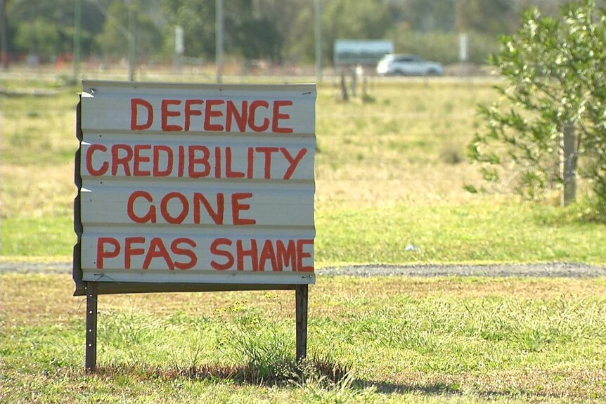 A sign reads "Defence Credibility Gone - PFAS Shame"