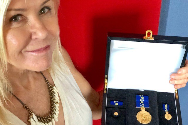A woman holds a box with gold medallions inside.