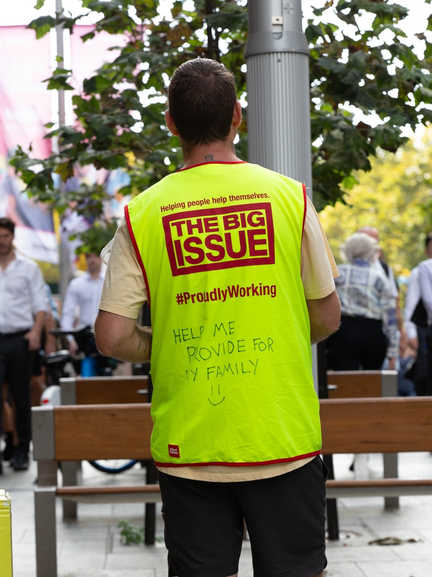 The back of a man wearing a hi-vis vest for The Big Issue with message 'help me provide for my family'