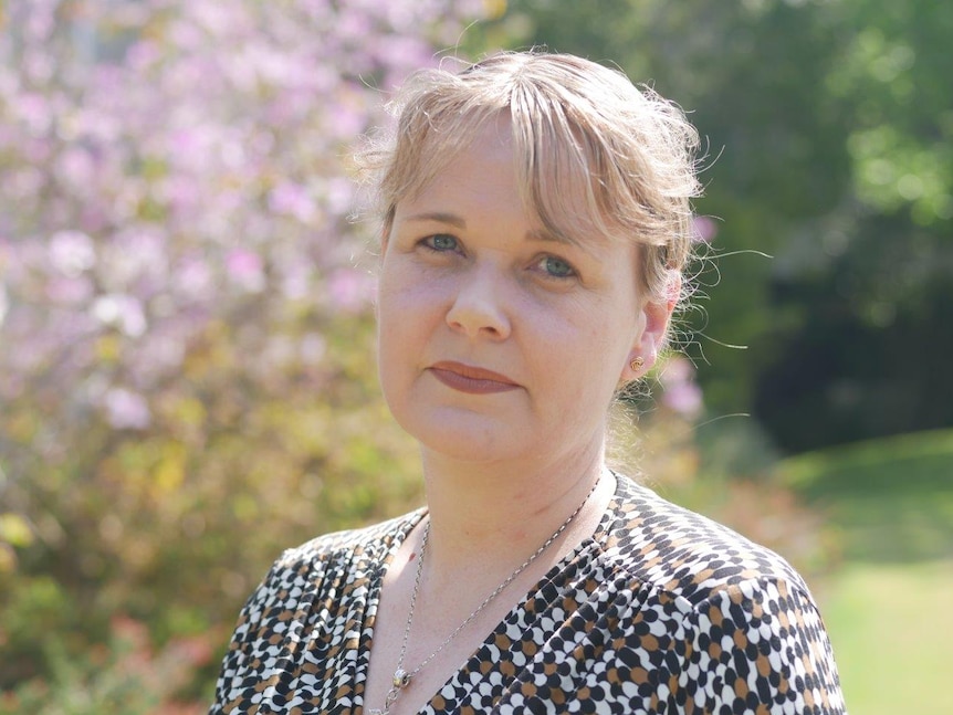 A close up photo of a woman standing outside in sunshine.