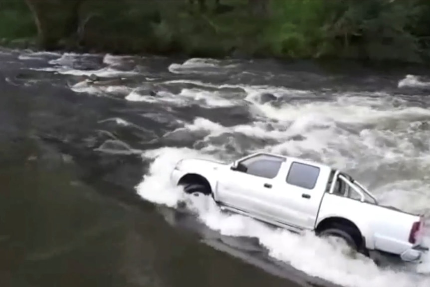A vehicle wedged sideways in fast flowing floodwaters.