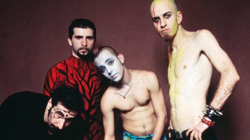 Four members of System of a Down, two of them shirtless, three of them with painted faces, one wearing a red & black turtleneck