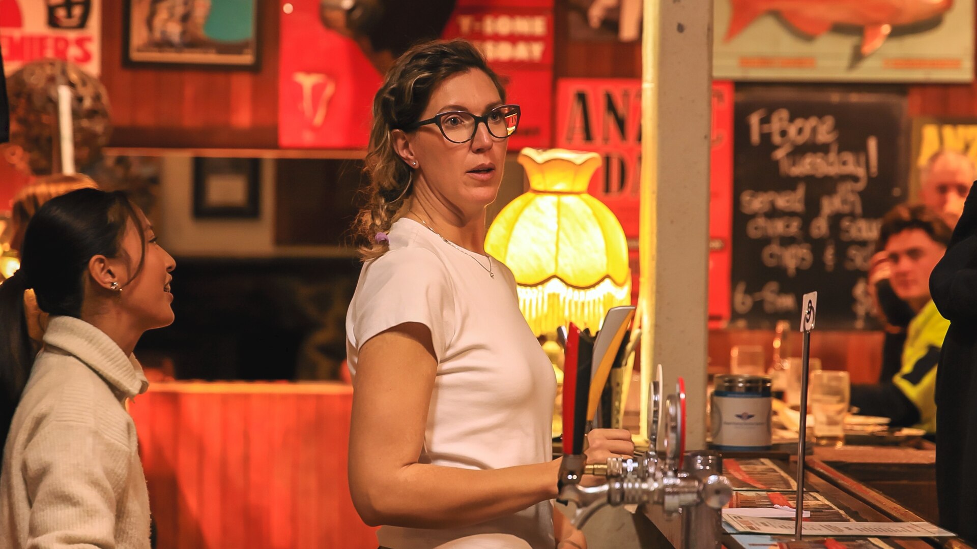 A slim woman with curly hair works behind a bar