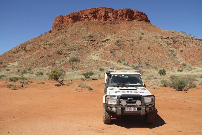 Police car parked in front of rocky outcrop.