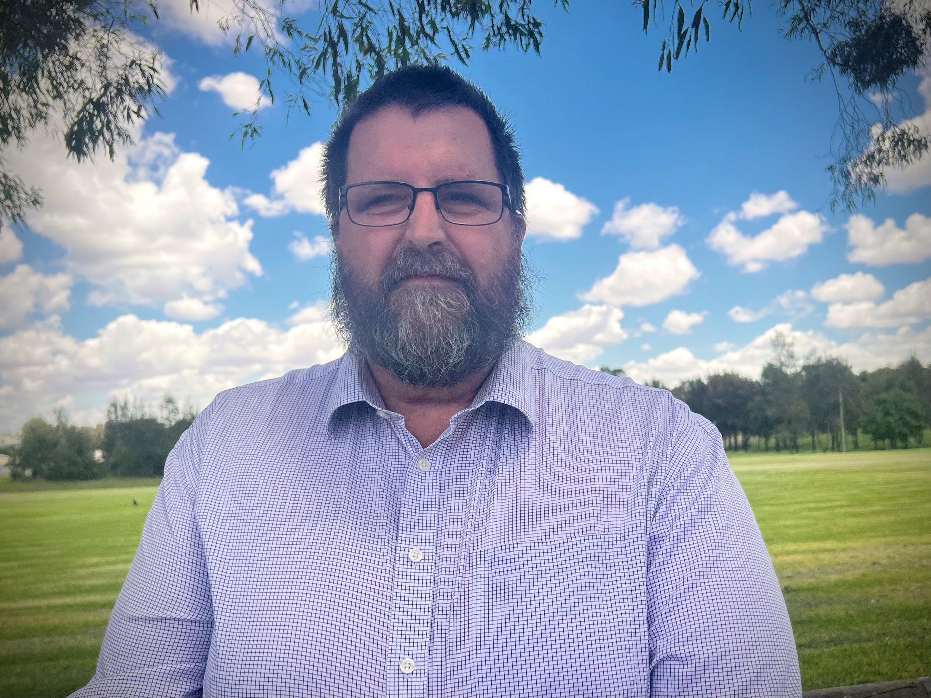 Troy Stolz está allí con camisa a cuadros y gafas, barba, cabello castaño y rostro serio.
