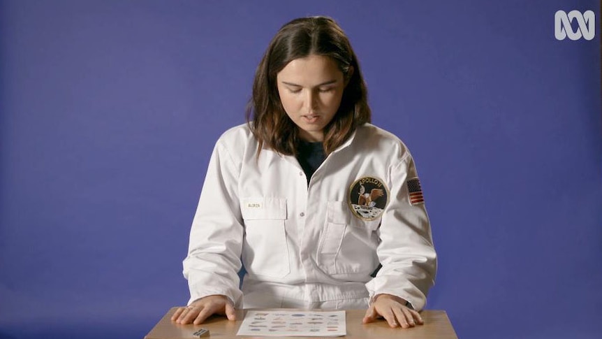Woman in astronaut overalls sits at table
