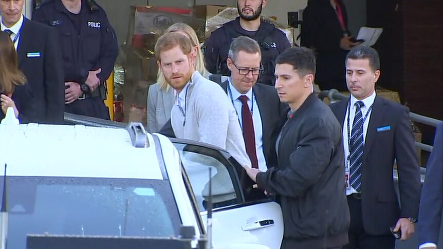 Prince Harry getting into a car with police in the background