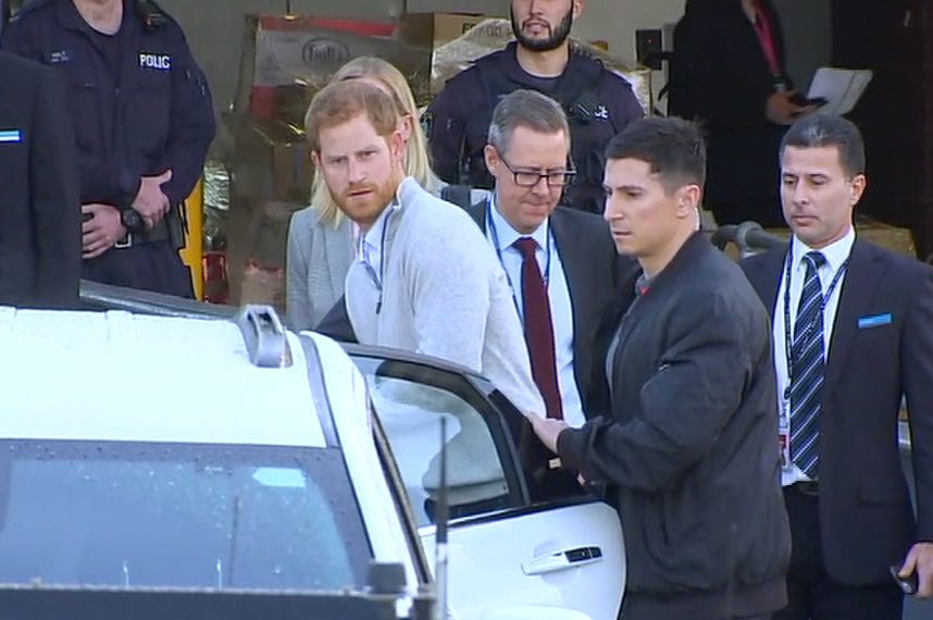 Prince Harry getting into a car with police in the background