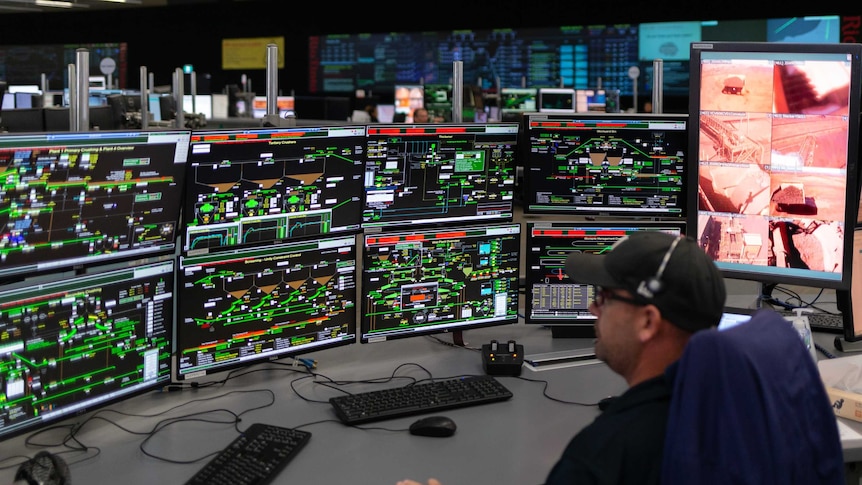 A man in a baseball cap sits in front of several screens displaying technical information at Rio Tinto's Operations Centre.