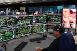 A man in a baseball cap sits in front of several screens displaying technical information at Rio Tinto's Operations Centre.