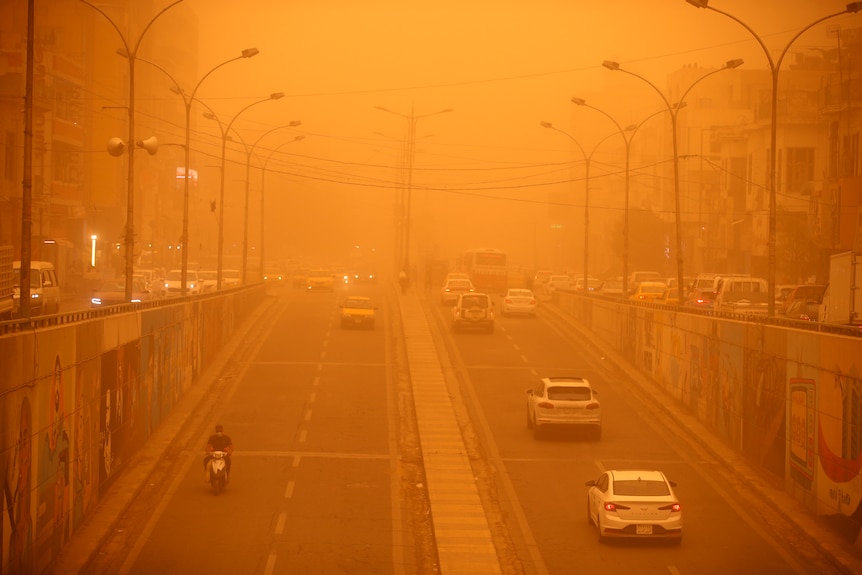 Vehicles drive along a road during a severe dust storm, which has left the sky orange. 