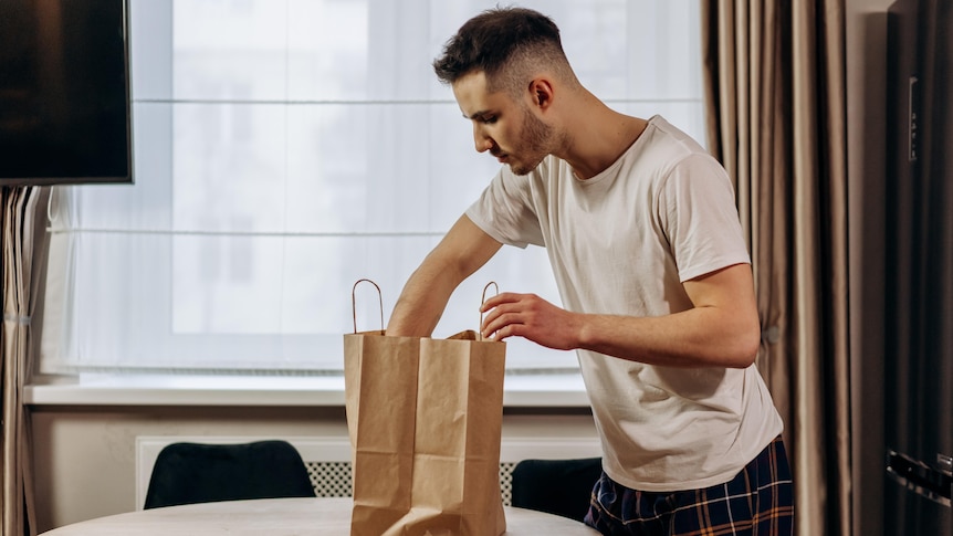 A man in a white shirt looks into a food delivery bag