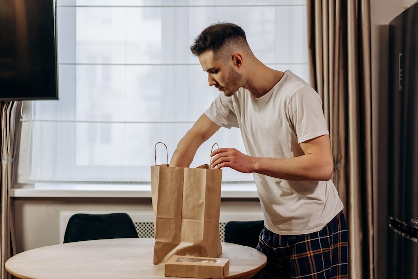 A man in a white shirt looks into a food delivery bag