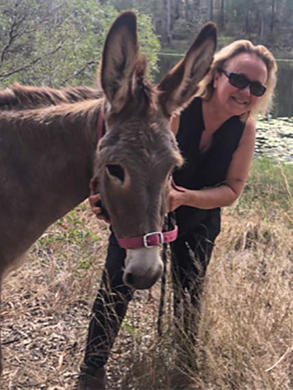 A smiling blonde woman posing with a donkey.