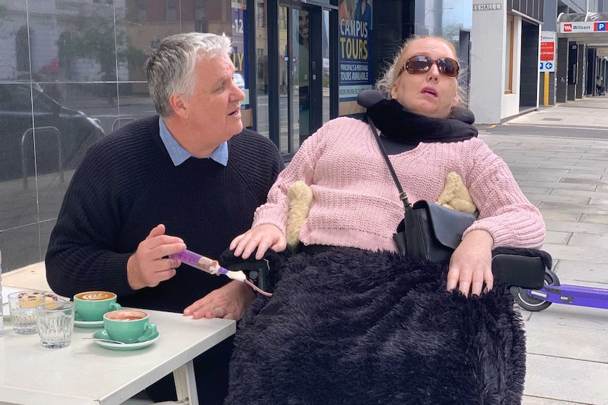 A carer helps to feed a woman with a disability.