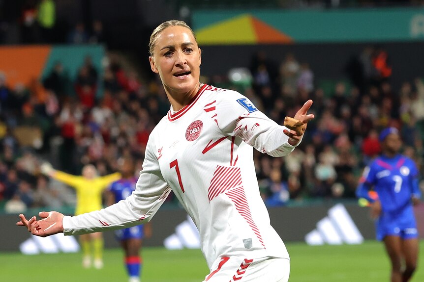 Sanne Troelsgaard raisers her arms in celebration on a soccer pitch
