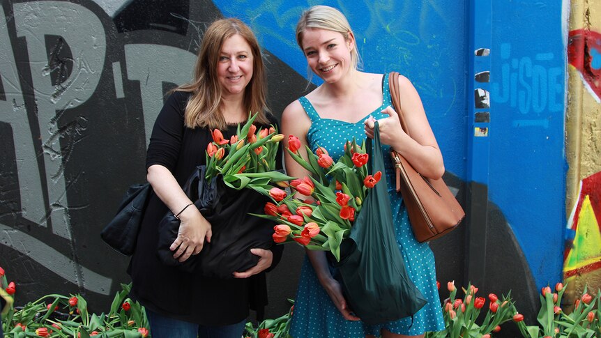 Colleagues Desi Assiminos and Steph Webb hold bags of tulips in front of the graffitied wall in Melbourne's Hosier Lane.
