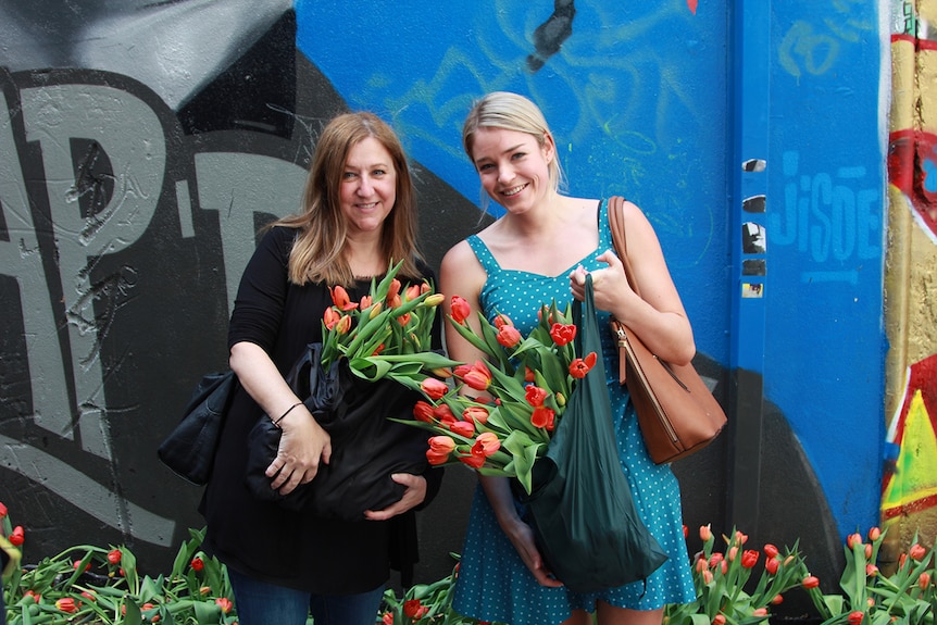 Colleagues Desi Assiminos and Steph Webb hold bags of tulips in front of the graffitied wall in Melbourne's Hosier Lane.