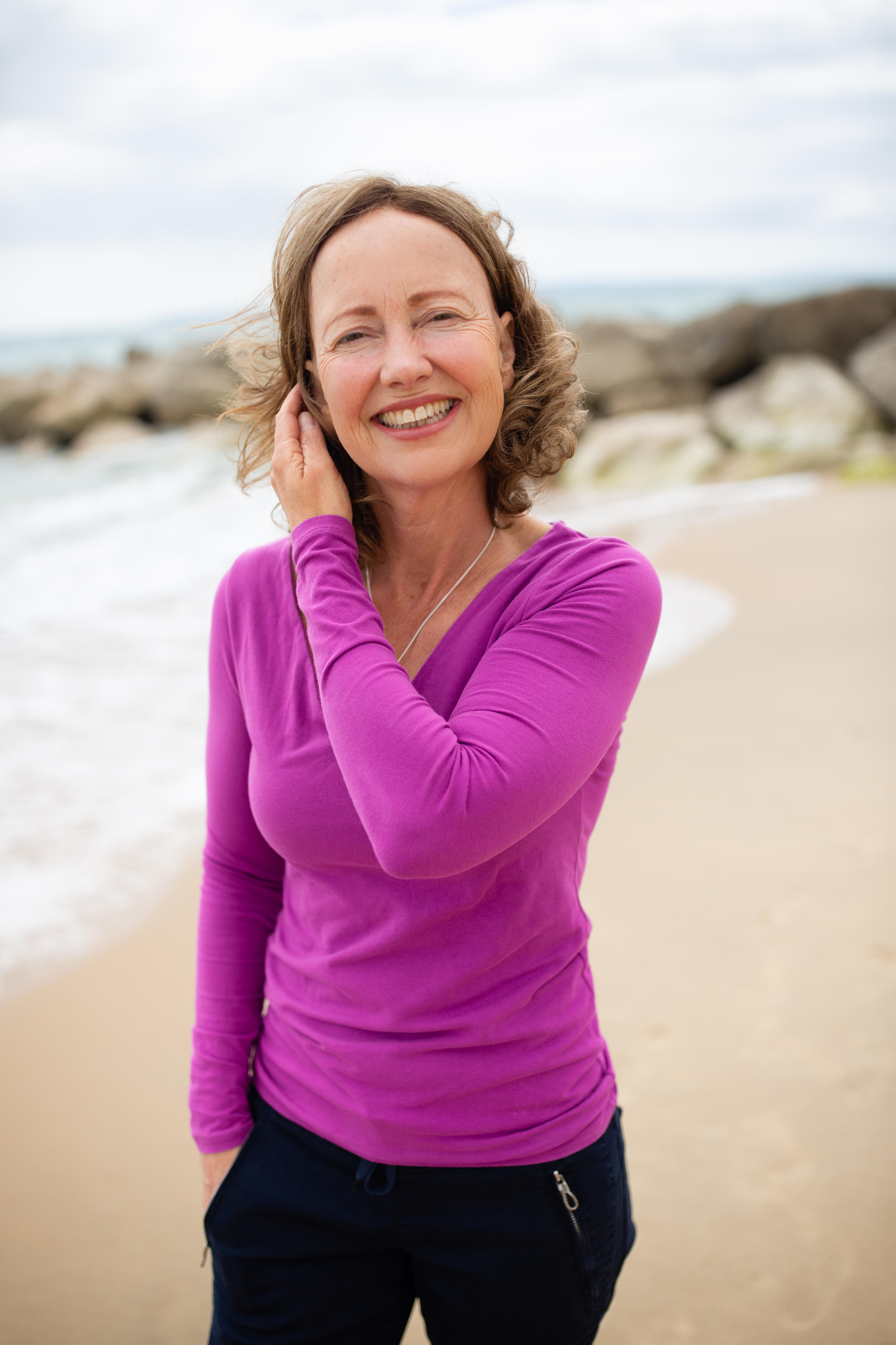 Katherine Baldwin smiles on the beach while tucking hair behind her ear