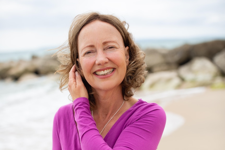 Katherine Baldwin smiles on the beach while tucking hair behind her ear