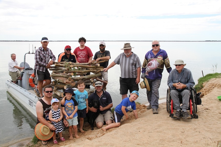 A group of people standing at the water's edge and on a boat.