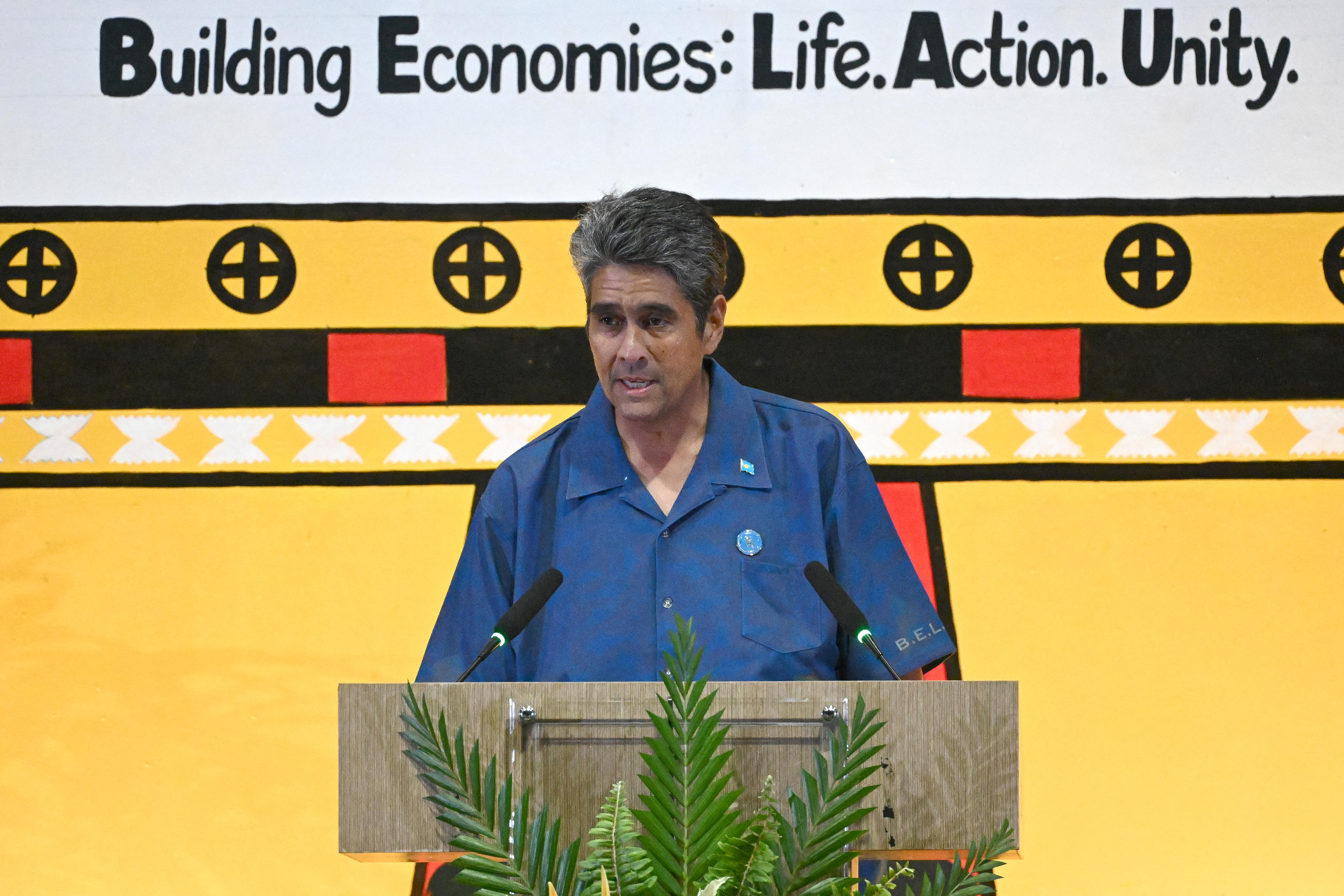 A man, wearing a blue shirt, stands behind a lectern.