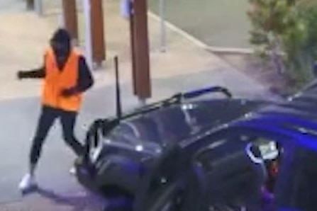 A person wearing a high-vis vest over dark clothes on the move outside a shopping centre.