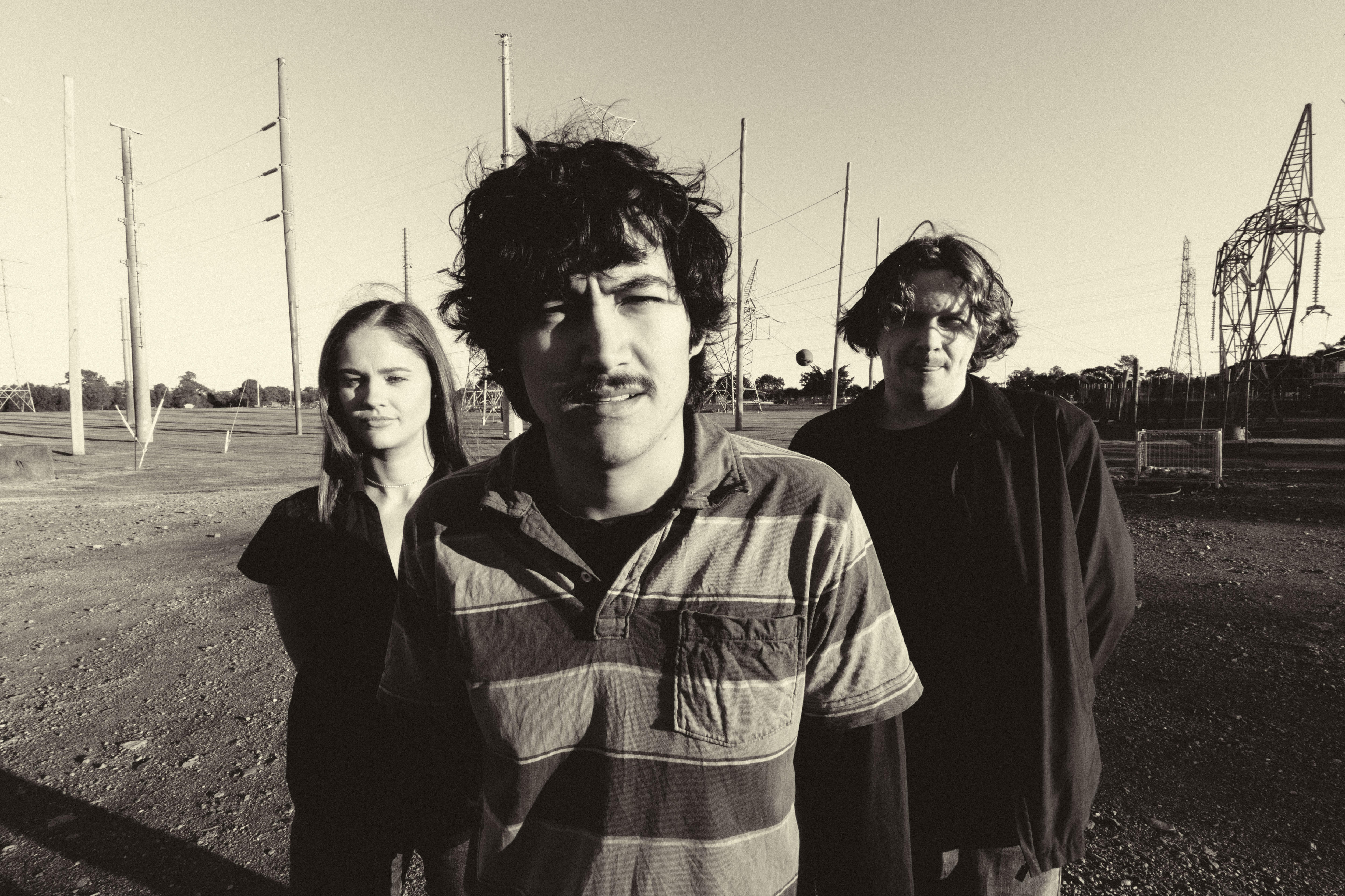 Monochrome image of three people in an open space with power lines and metal structures behind them