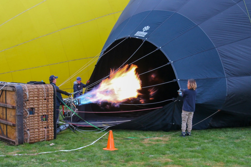 Three people holding hot a air balloon as it is inflated. 