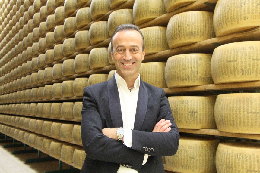 Man in front of wall of Parmigiano cheese wheels.
