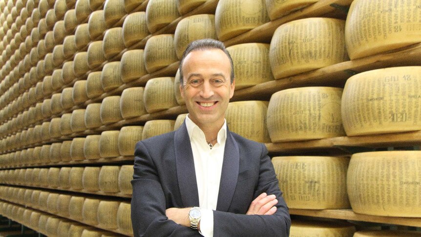 Man in front of wall of Parmigiano cheese wheels.