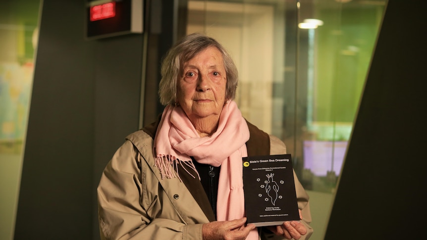 Aunty Barbara Nicholson standing in front of the ABC studios holding the Sistas Green Sea Dreaming book