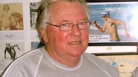 Man with grey hair and glasses, standing in front of a wall full of old photographs