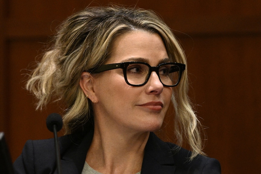 A close up of Dr Shannon Curry with blonde hair tied back and wearing black reading glasses looking away from the camera
