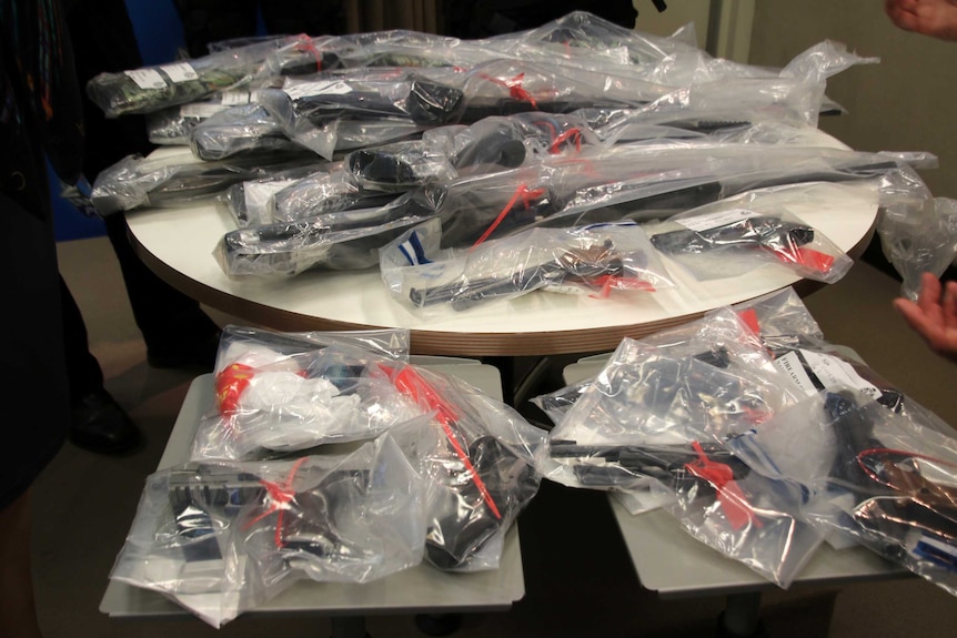 A close-up shot of three small tables covered in guns in plastic bags.