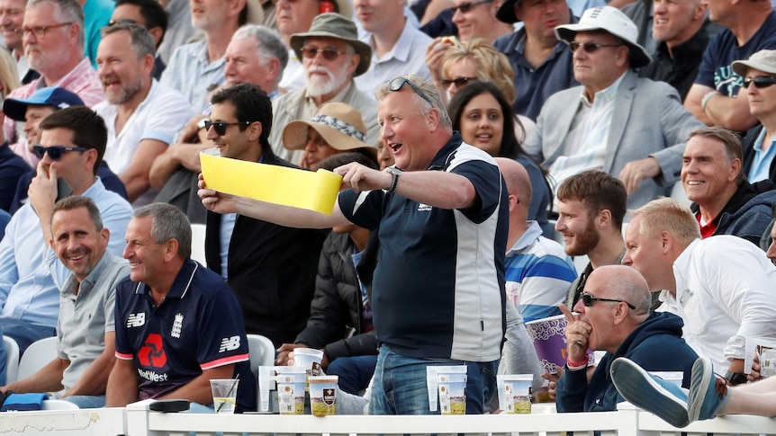 An England fan stands up and waves a piece of yellow sandpaper