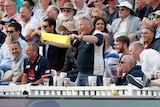 An England fan stands up and waves a piece of yellow sandpaper